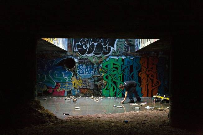 Graffiti artist Ruckoh reaches for a can of spray paint in a pool of water in a storm drain lit by a street grate almost directly under the Las Vegas Strip. 