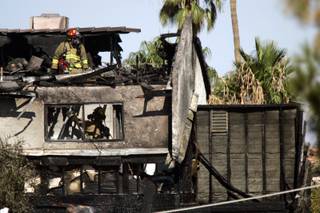 Firefighters look for hot spots after a twin-engine Piper Navajo crashed into a home on North Jones Boulevard near Cheyenne Avenue today. 