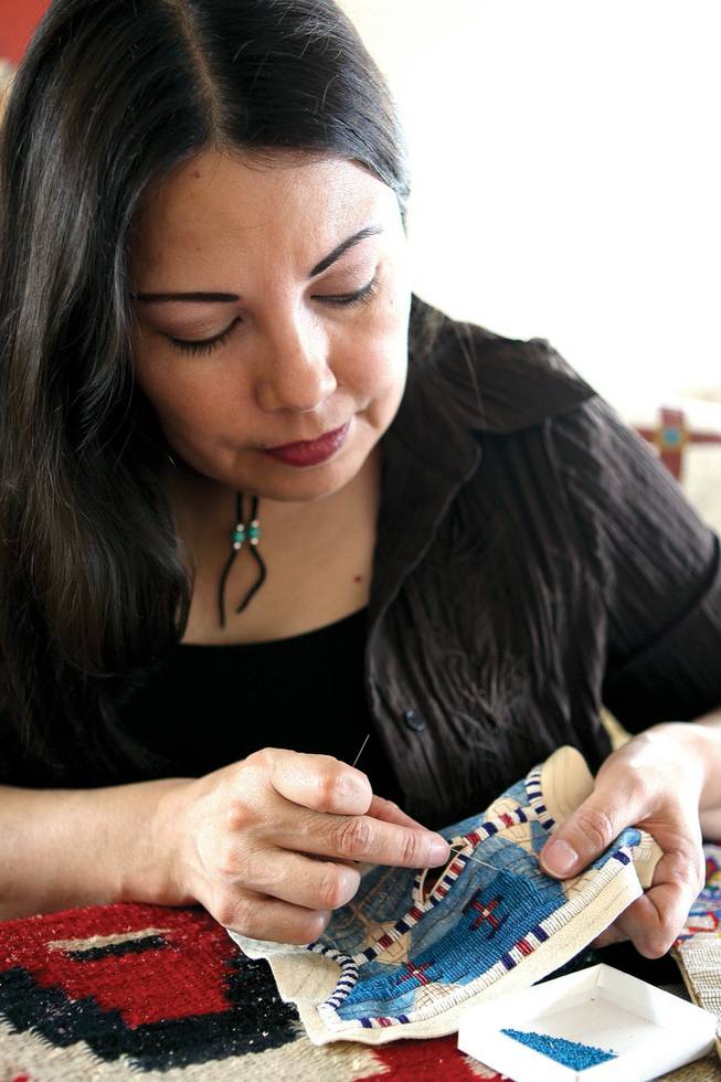Working with antique miniature beads, American Indian artist Rhonda Holy Bear beads fine lines of turquoise on a shawl for a doll.
