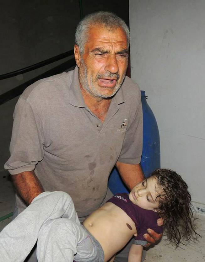 This citizen journalism image provided by the Local Committee of Arbeen which has been authenticated based on its contents and other AP reporting, shows a Syrian man reacts as he carries a dead body of a Syrian girl, after an alleged poisonous gas attack fired by regime forces, according to activists in Arbeen town, Damascus, Syria, Wednesday, Aug. 21, 2013.