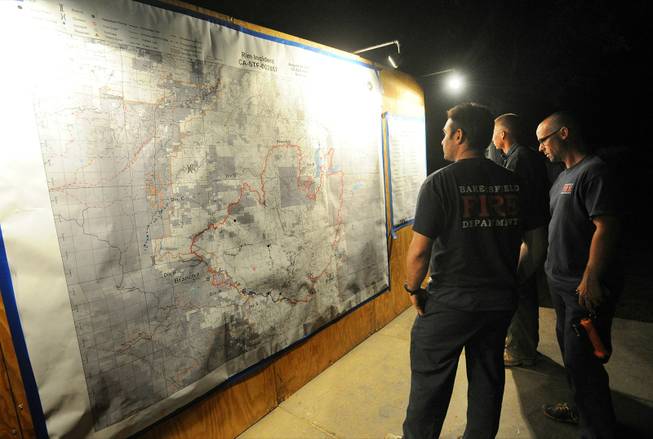 A trio of Bakersfield firefighters check an updated Rim Fire incident report map that is posted at the incident command post 7 miles east of Groveland, after a long hard day of fighting the fire, which continues to conflagrate uncontrolled in the Stanislaus National Forest Saturday Aug. 24, 2013.