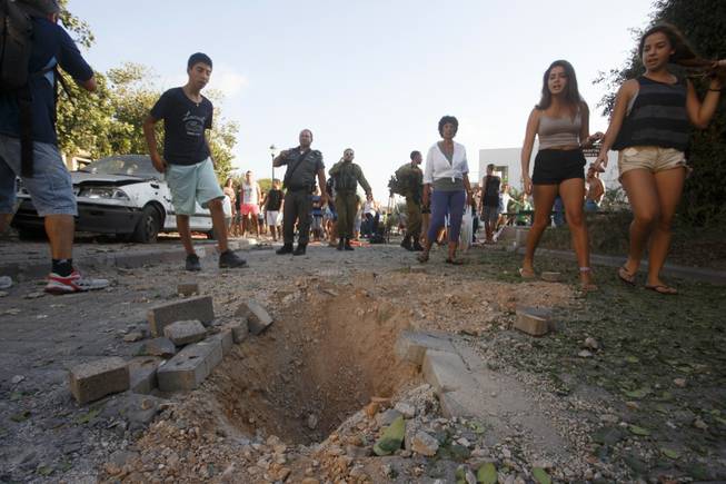 Israelis look at the crater caused by the impact of a rocket fired from Lebanon in kibbutz Gehser HaZiv outside Nahariya in northern Israel, Thursday, Aug. 22, 2013. Military spokesman Lt. Col. Peter Lerner said Thursday that three rockets landed in northern Israel, while one was shot down.