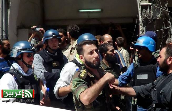 In this citizen journalism image provided by the United media office of Arbeen which has been authenticated based on its contents and other AP reporting, UN investigation team with blue helmets, walk with Syrian rebels in Damascus countryside of Zamalka, Syria, Wednesday, Aug. 28, 2013.