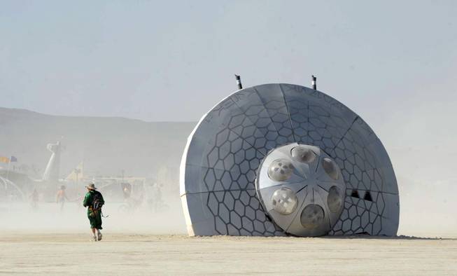 In this Thursday, Aug. 29, 2013 photo, a man walks past an art piece at Burning Man in Gerlach, Nev. Once a year, tens of thousands of participants gather for Burning Man in Nevada's Black Rock Desert to create Black Rock City, dedicated to community, art, self-expression and self-reliance.
