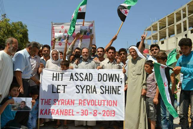 This citizen journalism image provided by Edlib News Network, ENN, which has been authenticated based on its contents and other AP reporting, shows anti-Syrian regime protesters holding a banner and Syrian revolution flags, during a demonstration in Kafr Nabil in Idlib province, northern Syria, Friday, Aug. 30, 2013.