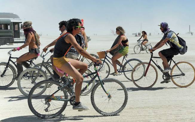 In this Thursday, Aug. 29, 2013 photo, people ride their bikes at Burning Man in Gerlach, Nev. Once a year, tens of thousands of participants gather for Burning Man in Nevada's Black Rock Desert to create Black Rock City, dedicated to community, art, self-expression and self-reliance.