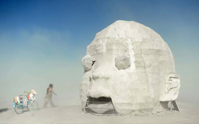 In this Thursday, Aug. 19, 2013 photo, Sam Ray visits the "Baby Head" art piece at Burning Man in Gerlach, Nev. Once a year, tens of thousands of participants gather for Burning Man in Nevada's Black Rock Desert to create Black Rock City, dedicated to community, art, self-expression and self-reliance.