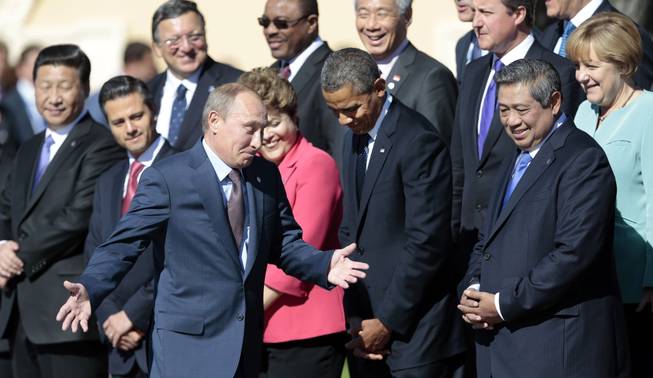 Russia's President Vladimir Putin, center foreground, gestures as he walks by U.S. President Barack Obama, front row second right, as he takes his place at a group photo outside of the Konstantin Palace in St. Petersburg, Russia on Friday, Sept. 6, 2013. World leaders are discussing Syria's civil war at the summit but look no closer to agreeing on international military intervention to stop it.