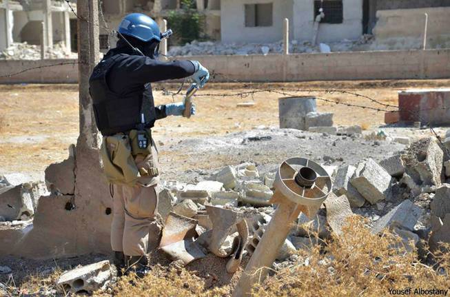 This citizen journalism image provided by the United media office of Arbeen which has been authenticated based on its contents and other AP reporting, shows a member of UN investigation team taking samples of sands near a part of a missile is likely to be one of the chemical rockets according to activists, in Damascus countryside of Ain Terma, Syria, Wednesday, Aug. 28, 2013. U.N. chemical weapons experts headed to a Damascus suburb on Wednesday for a new tour of areas struck by a purported poison gas attack, activists said, as Western powers laid the groundwork for a possible punitive strike and the U.N. chief pleaded for more time for diplomacy.