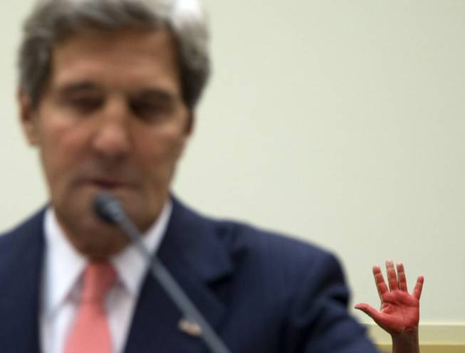 A protestors holds up their red painted hand behind Secretary of State John Kerry as he testifies on Capitol Hill in Washington, Wednesday, Sept. 4, 2013, before the House Foreign Affairs Committee hearing to advance President Barack Obama's request for congressional authorization for military intervention in Syria, a response to last month's alleged sarin gas attack in the Syrian civil war.