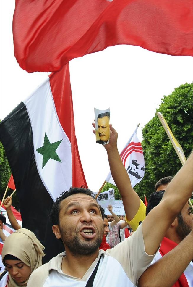 A demonstrator looks up during a rally against a possible U.S strike on Syria, Tuesday, Sept.10, 2013 in Tunis. U.S. President Barack Obama is going to Congress on Tuesday with fresh hopes of a diplomatic breakthrough that would allow Syria's government to avoid U.S. missile strikes if it surrenders its chemical weapons arsenal. Picture at center shows Syrian President Bashar Assad.