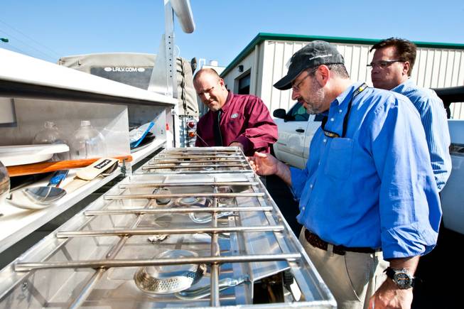 Rick Nelson (left), Land Rover event and social media director, displays a propane-fueled cooktop in the back of the 1997 Land Rover Defender to Matt Hufman and Mike Smith, right, as they prepare to explore Nevada over the next year working on the Finding Nevada Project at the Land Rover Las Vegas dealership Friday, September 13, 2013.