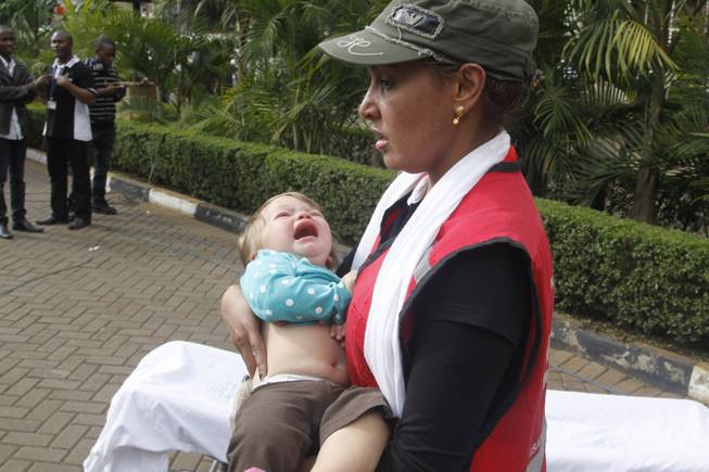 A Red Cross assistant helps a child outside the Westgate Mall in Nairobi, Kenya Saturday, Sept. 21, 2013, after gunmen threw grenades and opened fire during an attack that left multiple dead and dozens wounded. A witness to the attacks on the upscale shopping mall says that gunmen told Muslims to stand up and leave and that non-Muslims would be targeted.