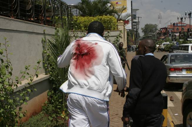 A wounded man is escorted outside the Westgate Mall, an upscale shopping mall in Nairobi, Kenya Saturday Sept. 21 2013, where shooting erupted when armed men attempted to rob a shop, according to police. Witnesses say a half dozen grenades also went off along with volleys of gunfire in and around the mall.
