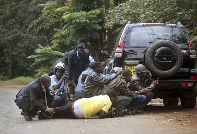 Kenyan security personnel and journalists duck behind a vehicle as heavy gunfire erupts from the Westgate Mall in Nairobi Kenya Monday Sept. 23 2013. Multiple large blasts have rocked the mall where a hostage siege is in its third day. Associated Press reporters on the scene heard multiple blasts and a barrage of gunfire. Security forces have been attempting to rescue an unknown number of hostages inside the mall held by al-Qaida-linked terrorists.