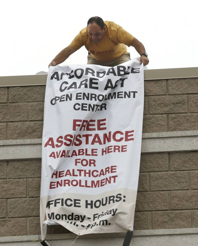 ACCESS Community Health and Research Center employee Salim Kazan unfurls an Affordable Care Act banner he is posting at the center in Dearborn, Mich., Tuesday, Oct. 1, 2013. Tuesday is the first day to shop on Michigans new insurance market created under the federal health care law.