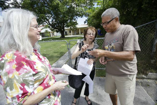Jane Townsend, left, and Hinda Cantor, center, volunteers with Enroll America, a private, non-profit organization running a grassroots campaign to encourage people to sign up for health care offered by the Affordable Care Act, talk with Elieas, right, who did give his last name, about his health care options as they canvassed a neighborhood, Tuesday, Oct. 1, 2013 in Miami. After months of build-up, Florida residents can start shopping for health insurance on government-run online marketplaces as the key component of the Affordable Care Act goes live.
