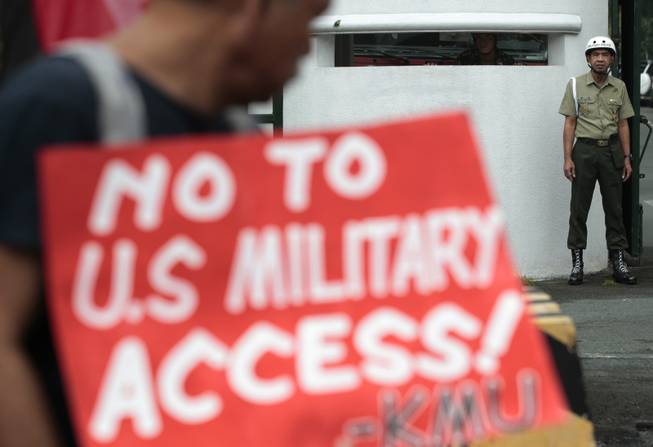 A Filipino protester looks at a military police stand guard outside the gate of he Camp Aguinaldo military headquarters in suburban Quezon city, north of Manila, Philippines on Tuesday Oct. 1, 2013. The group staged a rally opposing current negotiations to have larger U.S. military presence in the country. They are preparing for more protests in time for the planned visit of Obama this month.
