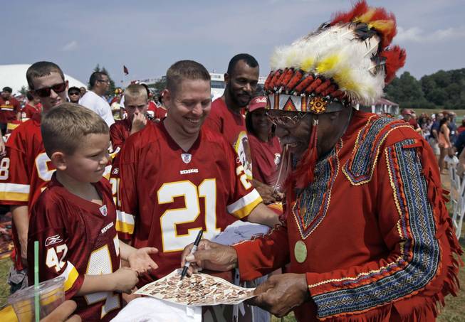 In this Saturday, Aug. 4, 2012, file photo, Zena "Chief Z" Williams, unofficial mascot of the Washington Redskins, signs autographs during fan appreciation day at the Redskins' NFL football training camp at Redskins Park in Ashburn, Va. The name Washington Redskins has inspired protests, hearings, editorials, lawsuits, letters from Congress, even a presidential nudge. Yet behind the headlines, it’s unclear how many Native Americans think “Redskins” is a racial slur.