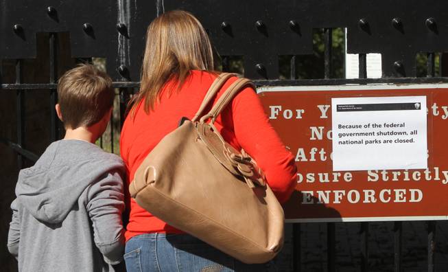 In this photo taken Friday, October 11, 2013, Susan Brinn and her son Cooper, both visiting from Nashville, examine a sign that reads "Because of the federal government shutdown, all national parks are closed." on the locked gate to Point Park in Lookout Mountain, Tenn. Point Park is in the Chickamauga and Chattanooga National Military Park, a Civil War battle park, parts of which are in Tennessee and Georgia.