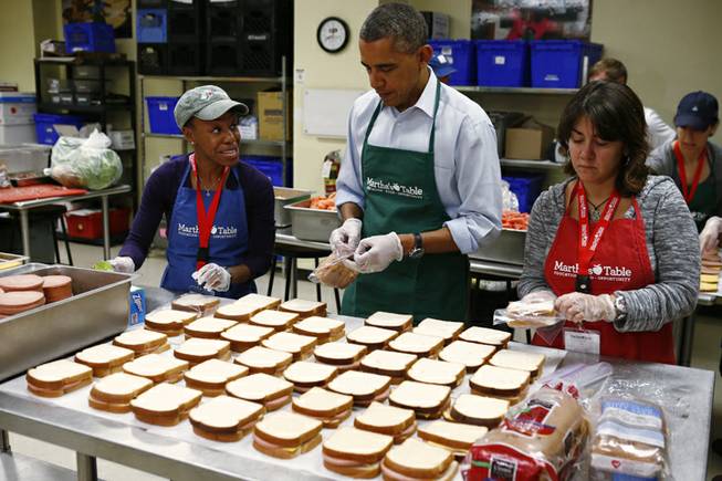 President Barack Obama puts sandwiches into bags with volunteers Dolly Garcia, who works at the US Census Bureau, right, and Chantelle Britton, who works at the Department of Health and Human Services, left, as he visits Martha's Table, which assists the poor and where furloughed federal employees are volunteering, in Washington, Monday, Oct. 14, 2013.