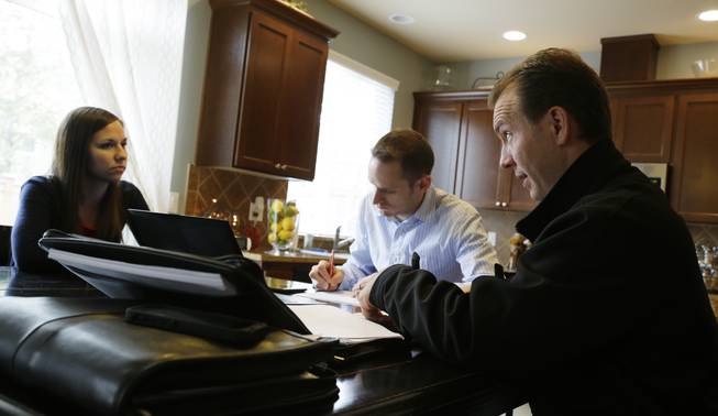 In this Thursday, Oct. 10, 2013, photo, insurance broker Jeff Lindstrom, right, meets with Brandi and Darren Litchfield to discuss health insurance plan options, at their home in the Seattle suburb of Bothell, Wash. Darren works for a startup company that doesn't yet offer an employee insurance plan, so they invited Lindstrom to outline the options of different healthcare plans that he offers as a broker.