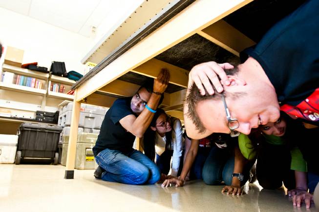 Graduate assistant Dev Raj Sharma (left) holds on while lab manager Chris Cothrun (right) covers his head while hovering under a table with other graduate assistants during the Great Nevada ShakeOut earthquake drill held in the Applied Geophysics Center at UNLV at 10:17 a.m. Thursday morning in Las Vegas, October 17, 2013.