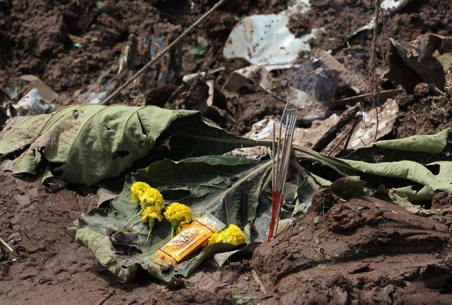 Flowers and incense sticks are offered beside the wreckage of an ill-fated Lao Airlines plane that chased on the riverbank and sank in the Mekong River in Pakse in Laos Thursday, Oct. 17, 2013. Rescuers in fishing boats pulled bodies from the muddy Mekong River on Thursday as officials in Laos ruled out finding survivors from a plane that crashed in stormy weather, killing 49 people from 11 countries.