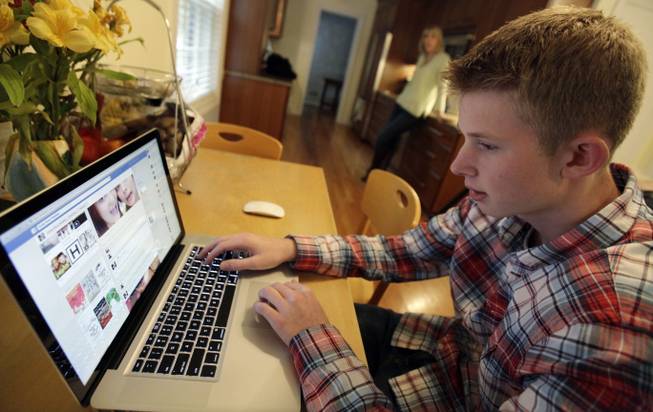 In this Oct. 24, 2013 photo, Mark Risinger, 16, checks his Facebook page on his computer as his mother, Amy Risinger, looks on at their home in Glenview, Ill. An influential pediatrician's group says unrestricted media use has been linked with violence, cyber-bullying, school woes, obesity, lack of sleep and a host of other problems. Mark’s mom said she agrees with restricting kids’ time on social media but that deciding on other media limits should be up to parents.