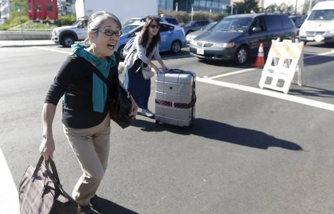 Gasaya Ichihara, left, runs across the street with her daughter, Sachika Ichihara, as they try to make their flight to Japan at Los Angeles International Airport on Friday, Nov. 1, 2013. Thousands of fliers were delayed Friday after a shooting in Terminal 3 closed parts of the airport for hours. Los Angeles police said a suspected gunman has been taken into custody. Los Angles is a major gateway for flights to Asia.