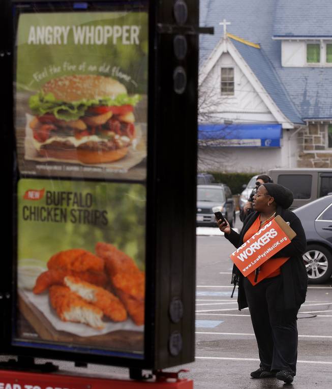 A woman participating in a demonstration outside a Burger King restaurant as part of a nation-wide protest supporting higher wages for workers in the fast-food industry and other minimum wage jobs listens to speakers while standing in the restaurant's parking lot in Boston, Thursday, Dec. 5, 2013. (AP Photo/Stephan Savoia)