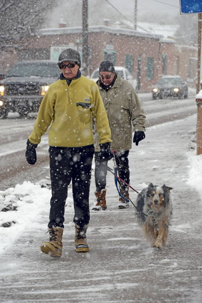 Melina and Gary Hall take a walk in the falling snow with their ten-year-old dog Roxie along the Old Santa Fe Trail in Santa Fe, N.M. Thursday, Dec. 5, 2013. Some northern New Mexico highways have difficult driving conditions Thursday as the latest blast of freezing temperatures, wind and snow causes delays and closures in parts of the state. National Weather Service forecasters say snowfall accumulations in some areas could reach 6 to 8 inches, with hardest-hit areas expected to include Torrance County and north toward Las Vegas.