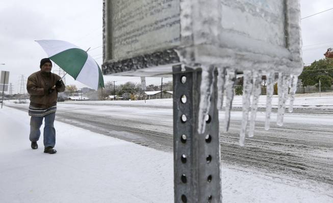 Joseph Mezo uses an umbrella as he walks to work in light sleet and icey conditions Friday morning, Dec. 6, 2013, in Dallas. An ice storm in North Texas has knocked out power to more than a quarter of a million homes and business, canceled almost 1,000 flights and contributed to a fatal wreck. The National Weather Service issued a winter storm warning for the Dallas area until Friday night.