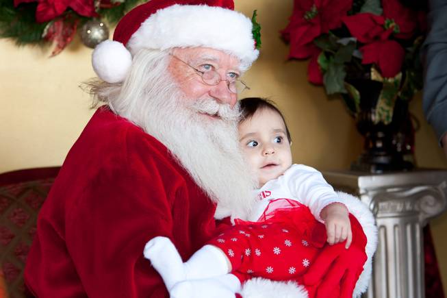 Visiting Santa for the first time, ten-month-old Annalisa Hamill smiles while having her picture taken in his cottage at Tivoli Village in Las Vegas Friday, December 13, 2013. Larry Hansen has been donning the coveted suit and sharing the spirit of Santa for over nine years in Las Vegas.
