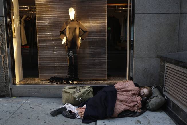 In this Wednesday, Nov. 20, 2013, file photo, a destitute man sleeps on the sidewalk under a holiday window at Blanc de Chine, in New York The growing gap between the richest Americans and everyone else isn’t bad just for individuals it’s hurting the U.S. economy says a majority of more than three dozen economists surveyed in December 2013 by The Associated Press.