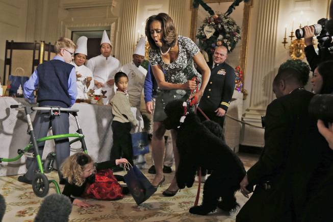 First lady Michelle Obama reacts as Ashtyn Gardner, 2, from Mobile, Ala., loses her balance when she was greeting Sunny, one of the presidential dogs, as children of military families participate in a holiday arts and crafts event in the State Dining Room at the White House in Washington, Wednesday, Dec. 4, 2013.
