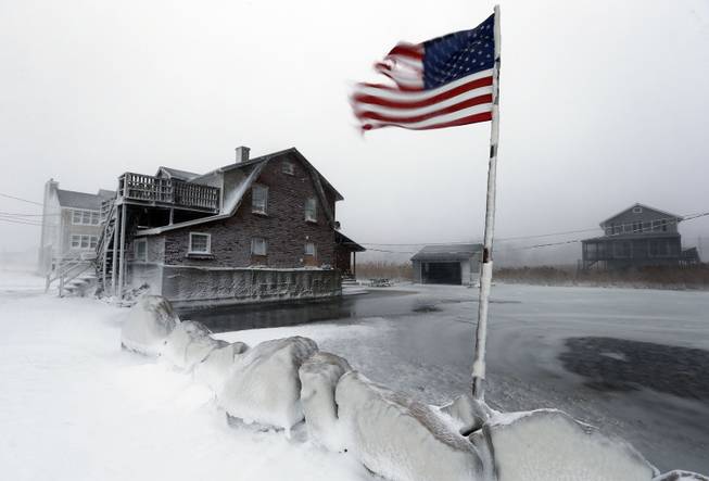 A tattered flag flies by a flooded yard along the shore in Scituate, Mass., Friday, Jan. 3, 2014. A blustering winter storm that dropped nearly 2 feet of snow just north of Boston, shut down major highways in New York and Pennsylvania and forced U.S. airlines to cancel thousands of flights nationwide menaced the Northeast on Friday with howling winds and frigid temperatures.