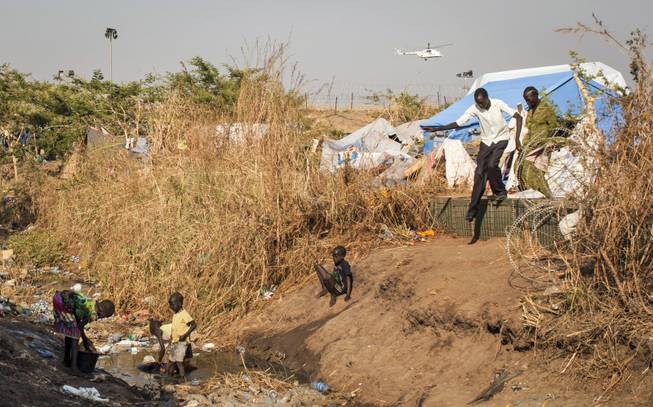 Young displaced children wash their clothes in a stream of fetid water that runs through a camp for people who have fled the recent violence, as a United Nations helicopter flies overhead in the distance, in the capital Juba, South Sudan Saturday, Jan. 11, 2014. South Sudanese government troops on Friday retook Bentiu, the capital of oil-producing Unity state, from rebels loyal to the country's former vice president, a military spokesman said, while hundreds of thousands remain displaced in the nearly monthlong conflict.