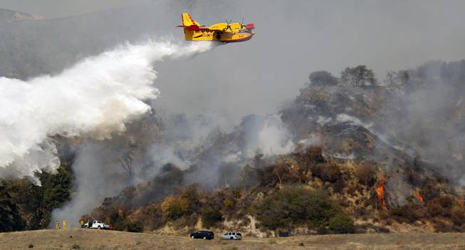 A firefighting plane makes a water drop on a wildfire that's burning in the hills just north of the San Gabriel Valley community of Glendora, Calif., on Thursday, Jan 16, 2014. Southern California authorities have ordered the evacuation of homes at the edge of a fast-moving wildfire burning in the dangerously dry foothills of the San Gabriel Mountains.
