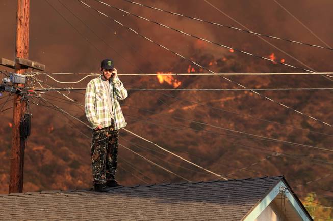 A resident on the roof of a house talks on the phone as a wildfire burns in the hills just north of the San Gabriel Valley community of Glendora, Calif. on Thursday, Jan 16, 2014. Southern California authorities have ordered the evacuation of homes at the edge of a fast-moving wildfire burning in the dangerously dry foothills of the San Gabriel Mountains.