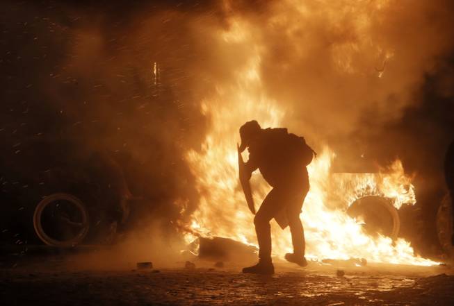 A protester throws a molotov cocktail towards a burning police car, in front of him, during clashes with police, in central Kiev, Ukraine, early Monday, Jan. 20, 2014. Anti-government protests in Ukraine's capital escalated into fiery street battles with police Sunday as thousands of demonstrators hurled rocks and firebombs to set police vehicles ablaze. Dozens of officers and protesters were injured.