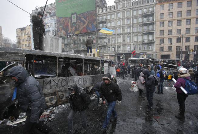People walk past the wreckage of vehicles, torched by protesters, after violent clashes in central Kiev, Ukraine, Tuesday, Jan. 21, 2014. Opposition leader Vitali Klitschko headed for talks with the Ukrainian president on Tuesday after yet another night of violent street clashes between anti-government protesters and police.