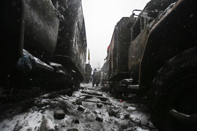 People walk between wreckage of vehicles torched by protesters overnight during violent clashes in central Kiev, Ukraine,Tuesday, Jan. 21, 2014. Opposition leader Vitali Klitschko headed for talks with the Ukrainian president on Tuesday after yet another night of violent street clashes between anti-government protesters and police.