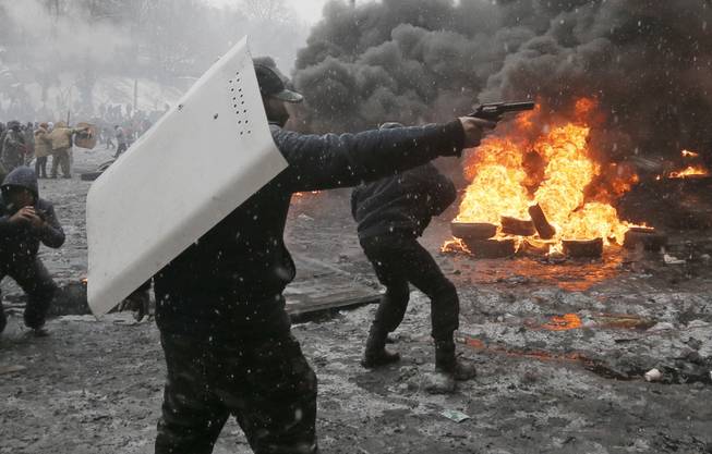 A protester points a handgun during a clash with police in central Kiev, Ukraine, Wednesday, Jan. 22, 2014. Three people have died in clashes between protesters and police in the Ukrainian capital Wednesday, according to medics on the site, in a development that will likely escalate Ukraine's two month-long political crisis.