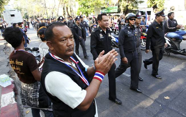 Anti-government protesters clap as Thai policemen walk in to take positions between pro- and anti-elections groups at Dindaeng district office in Bangkok, Thailand, on Sunday, Feb. 2, 2014. Thailand's tense national election got underway Sunday with protesters forcing the closure of several polling stations in the capital amid fears of more bloodshed a day after gun battles in Bangkok left seven people wounded.