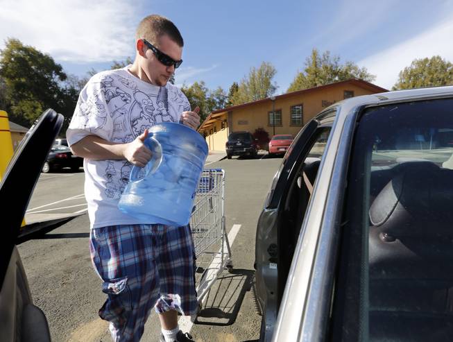 In this photo taken Tuesday, Feb. 4, 2014, Forrest Clark, 25, loads five gallon bottles of water, purchased at a local store, into his car in Willits, Calif. With local reservoirs holding less than a 100-day supply of water, city leaders have banned lawn watering, car washing and mandated all residents to cut water use. Clark, who said he doesn't like the taste of the local water, buys 10-15 gallons of bottled water a week to help boost the family water supply.