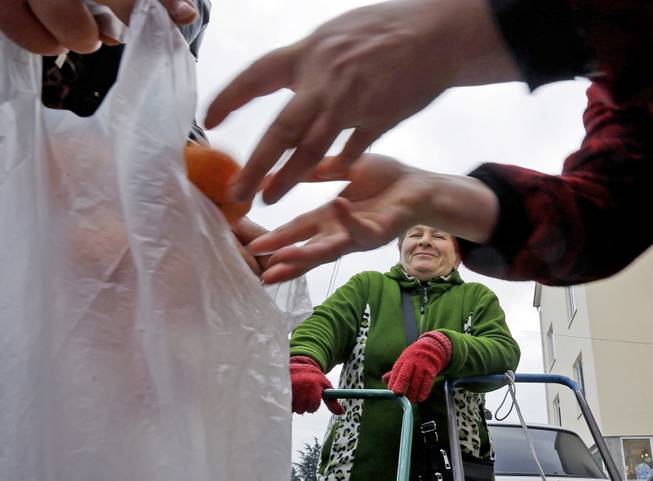 Mukhmunad Ashabokova watches as someone puts tangerines in a bag at the Abkhazian border Wednesday, Feb. 5, 2014, near Sochi, Russia. Most days in the tangerine season, she rolls her squat cart loaded down with the fruit across the bridge over Psou River from her garden about two miles inside Abkhazia.
