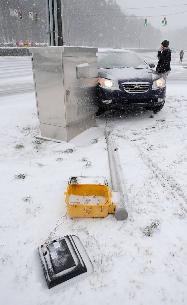 A motorist stands alongside his car after becoming lodged next to a mechanical box and lifted onto a cross walk signal Charlotte, N.C. on Wednesday, Feb. 12, 2014. North Carolina residents were bracing Wednesday for what forecasters were warning will be a serious winter storm that will cover much of the state in snow, sleet and ice.