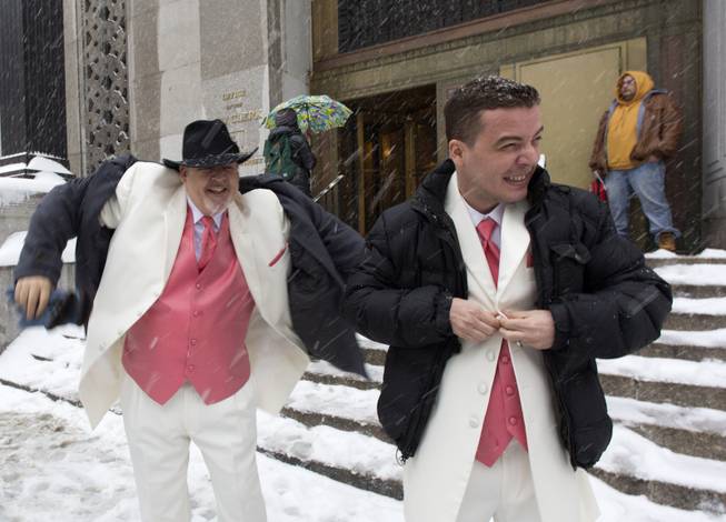 Newlyweds Steve Cosh, left, and Thiago Cardoso pull on their winter jackets as they step out from New York's municipal marriage bureau, Thursday, Feb. 13, 2014. Snow and sleet are falling on the East Coast from North Carolina to New England a day after sleet, snow and ice bombarded the Southeast.