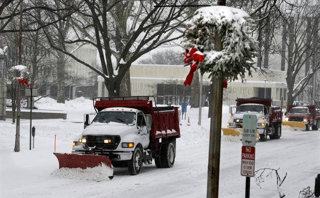 Snow plows drive past Christmas decorations in Trenton, N.J., Thursday, Feb. 13, 2014. After pummeling wide swaths of the Southeast, a winter storm dumped more than a foot of snow in parts of the Mid-Atlantic region as it marched Northeast and threatened more power outages, traffic headaches and widespread closures for millions of residents.